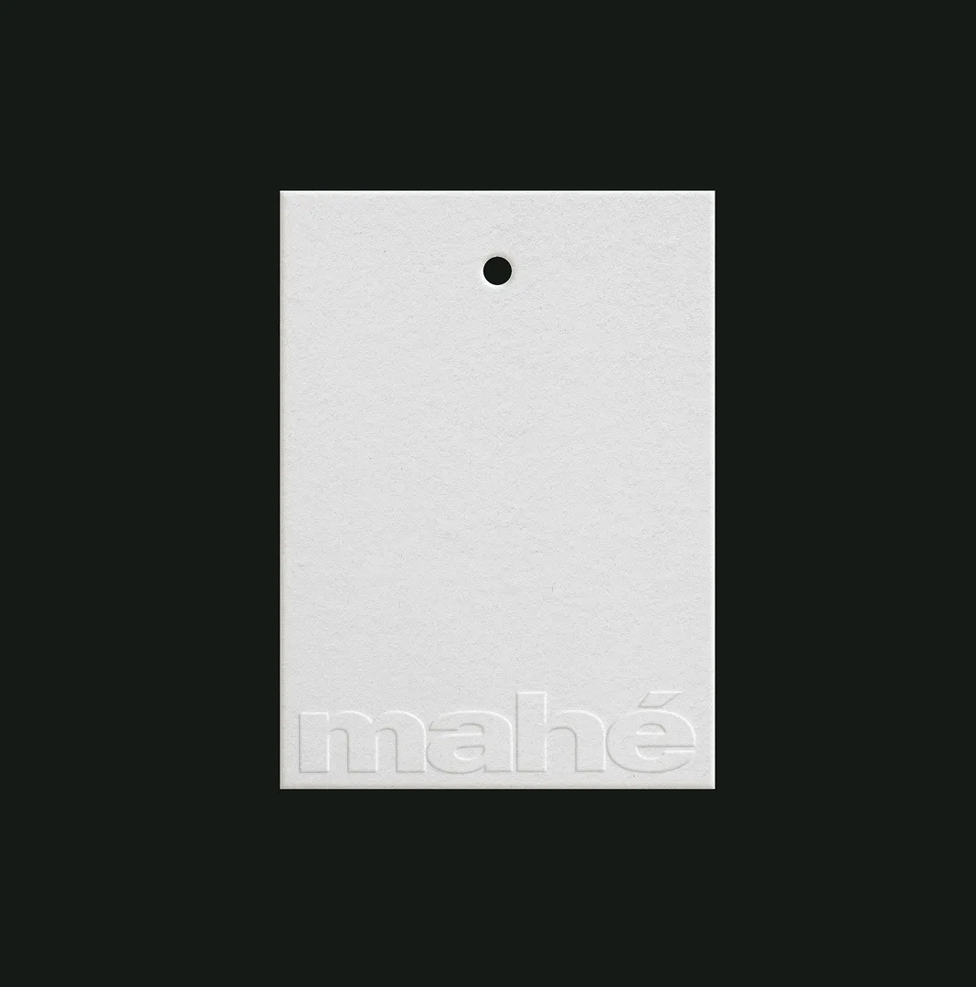 White hangtag with a blind-embossed mahé logo on a dark background